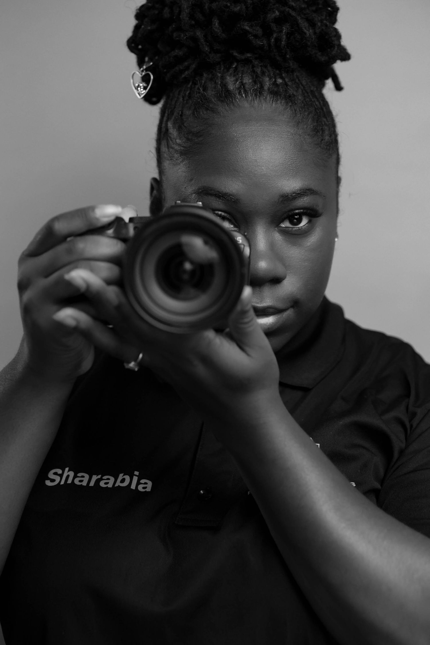 Black and white portrait of photographer Sharabia holding a DSLR camera up to her eye.