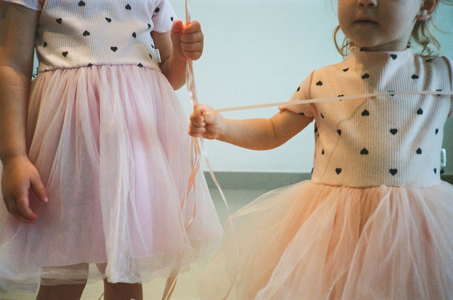 Two young girls in matching pink tulle skirts and heart-print tops holding wands outdoors.