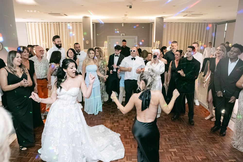 Bride in white gown dancing with guests at elegant wedding reception party on herringbone wood floor.