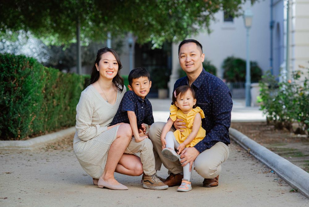 A family sits together on a concrete curb surrounded by greenery.