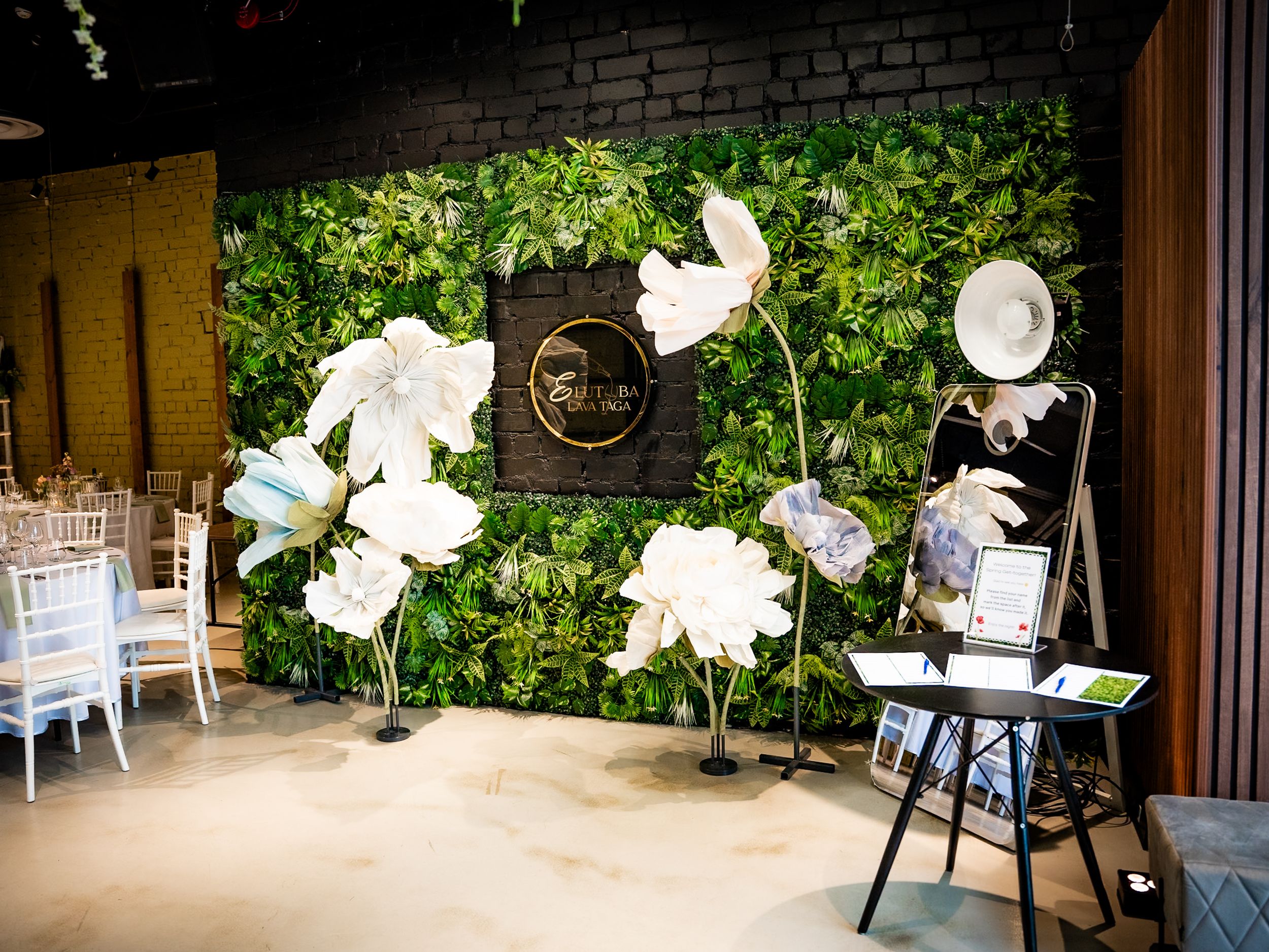 Elegant event space with lush green living wall, large white floral sculptures, and white chiavari chairs.