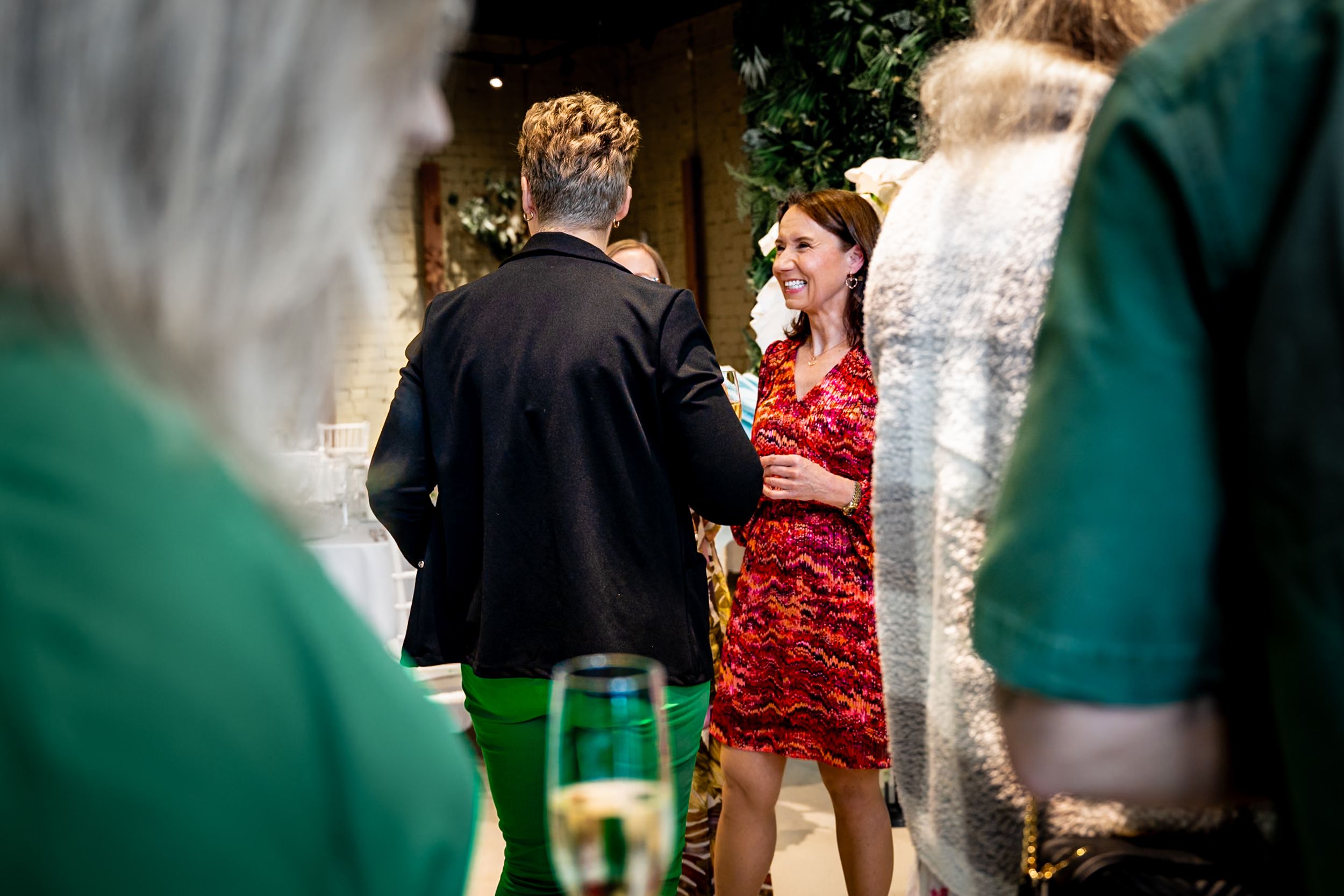 Woman in red floral dress smiling at a social gathering, holding a drink at an elegant indoor event.