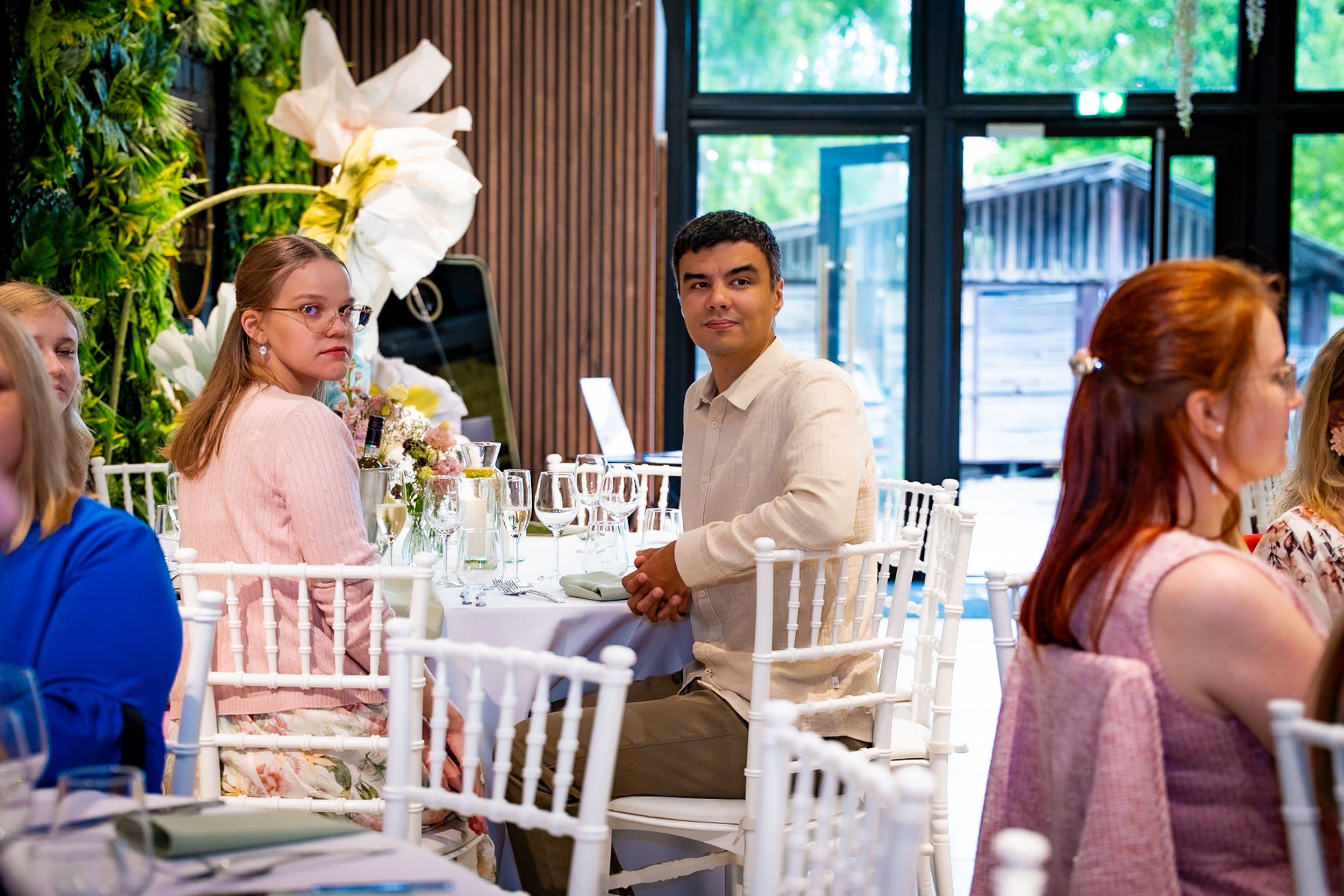 Guests in elegant attire socializing at a floral-decorated wedding reception in a bright, modern venue.