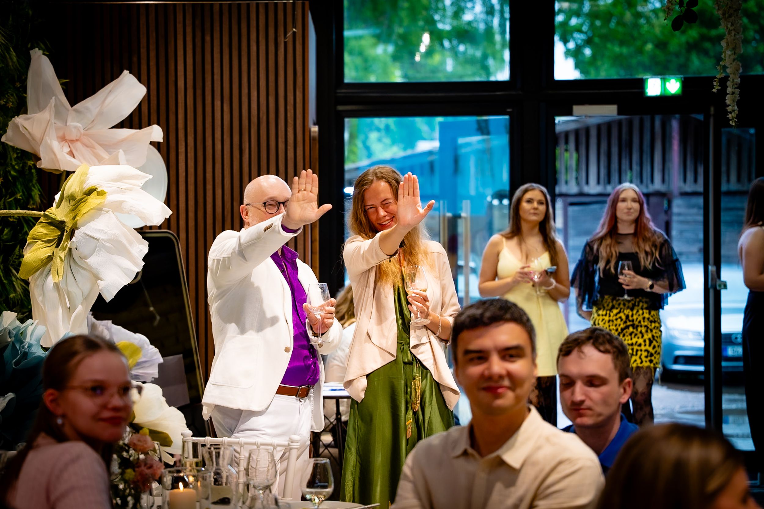 Priest in white vestments blesses guests at an elegant indoor wedding reception dinner celebration.