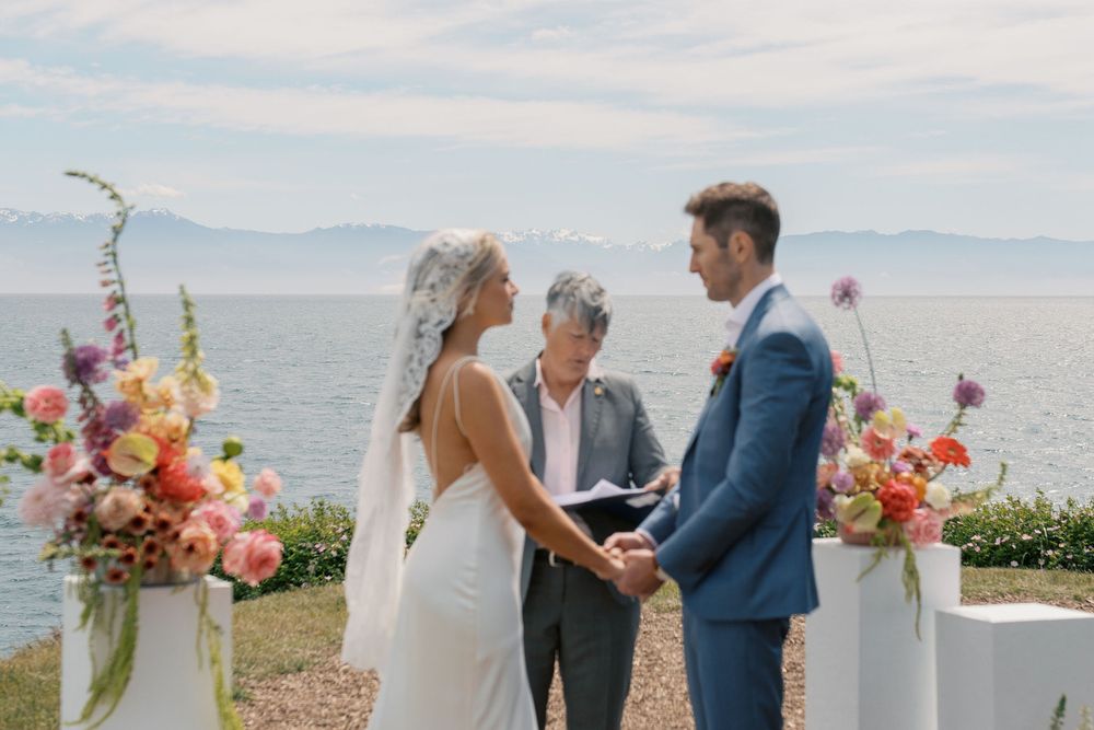 Couple exchanges vows at outdoor lakeside wedding ceremony with colorful floral arrangements and mountain views.