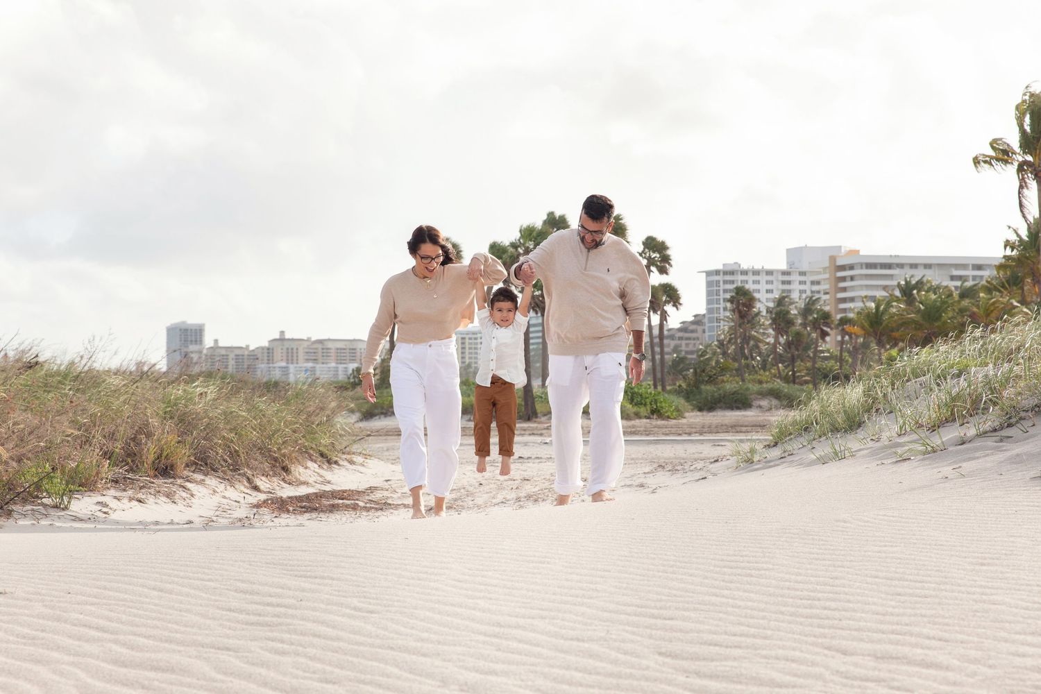 Family sitting together on beach at sunset wearing casual clothing.