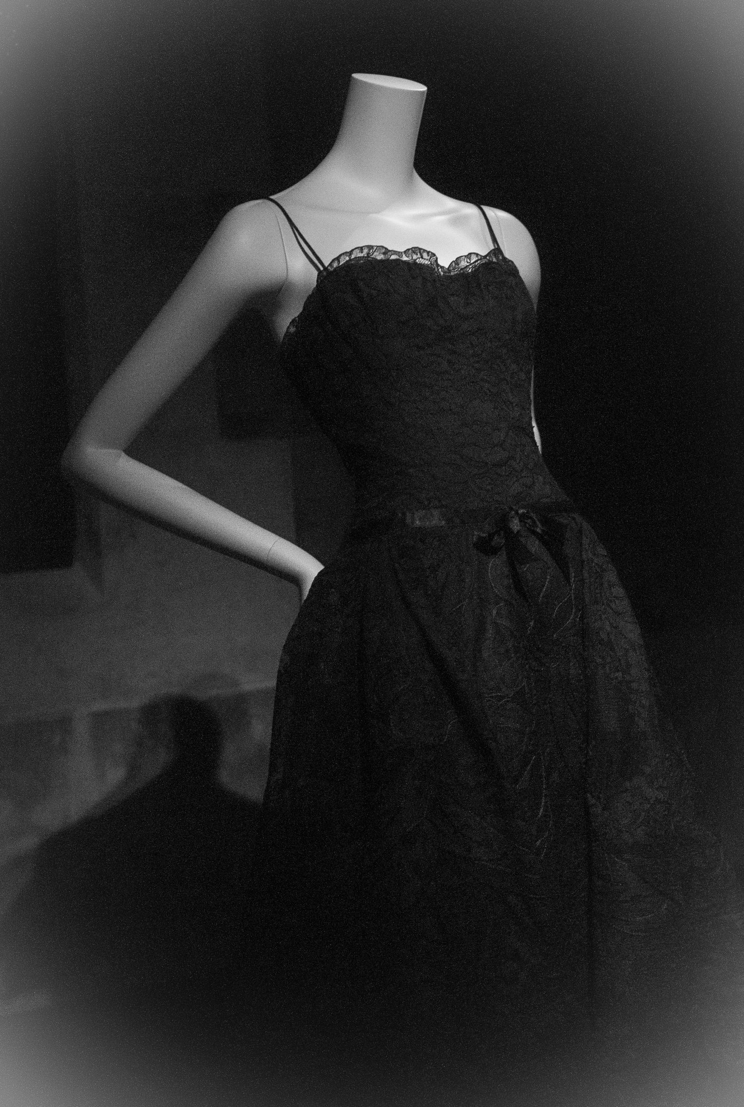 Black lace cocktail dress with spaghetti straps and bow waist on mannequin, elegant vintage style.