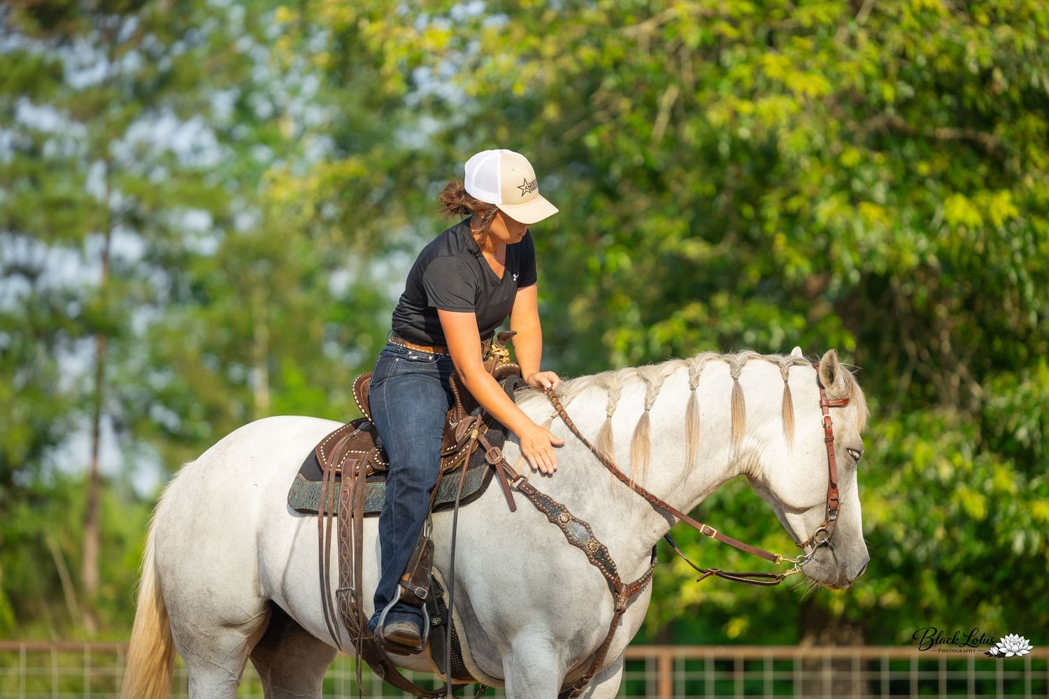 A young woman in a white cap rides a white horse in a lush green outdoor equestrian setting.