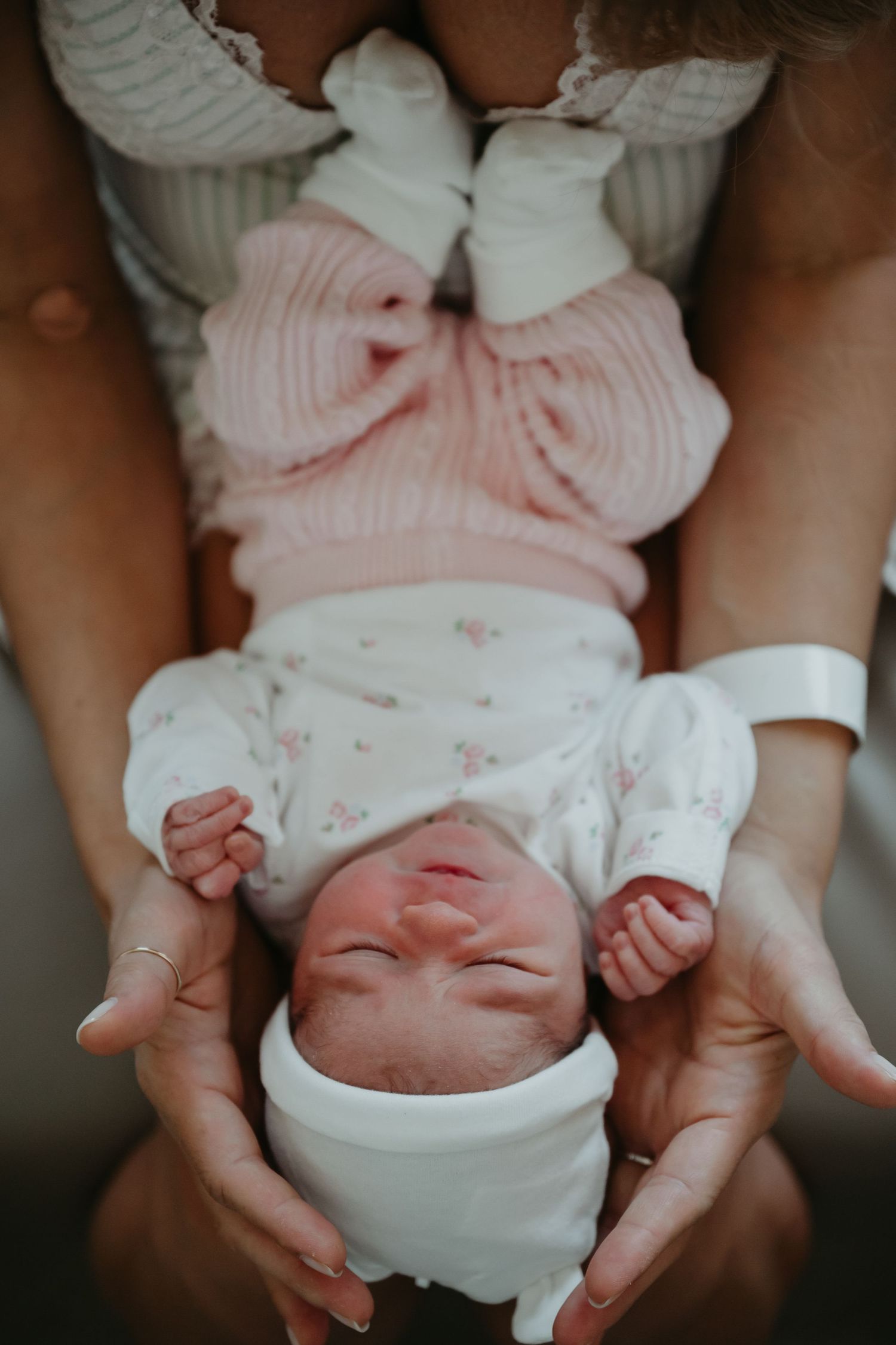 Newborn baby in pink and white outfit lying peacefully in parent's hands.