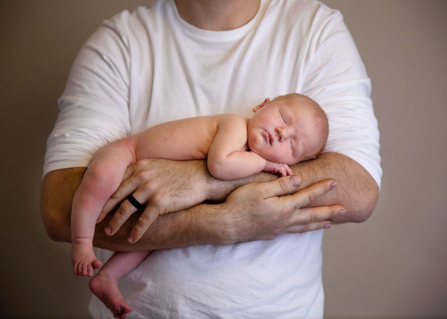 A newborn baby sleeping peacefully in the arms of an adult wearing a white t-shirt.
