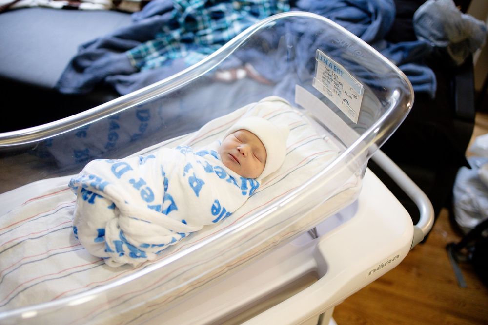 Newborn baby swaddled in blue and white blanket sleeping peacefully in a hospital bassinet.