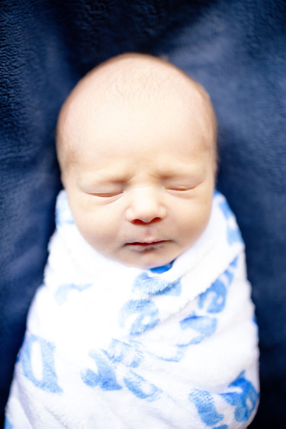 Peaceful newborn baby swaddled in a white and blue blanket, sleeping soundly against a dark blue background.