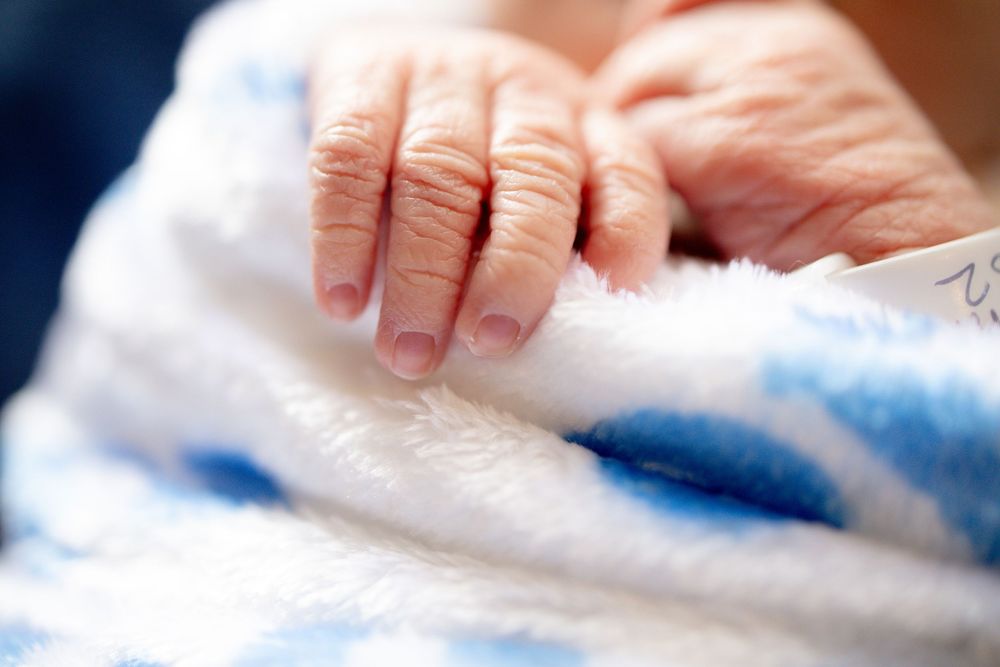 Close-up of an elderly person's wrinkled hand resting on a soft blue and white blanket.