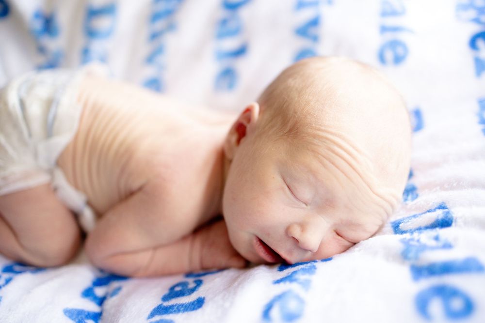 Newborn baby sleeping peacefully on a blue and white blanket, curled up in a cozy position.