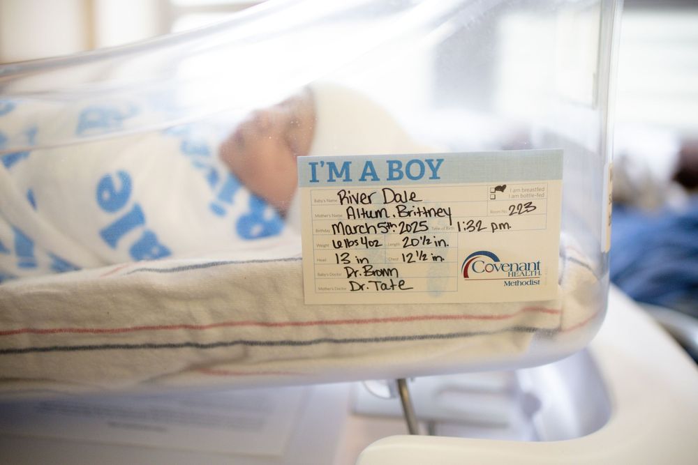 Newborn baby boy resting in hospital bassinet with blue name card reading I'm a Boy in maternity ward.