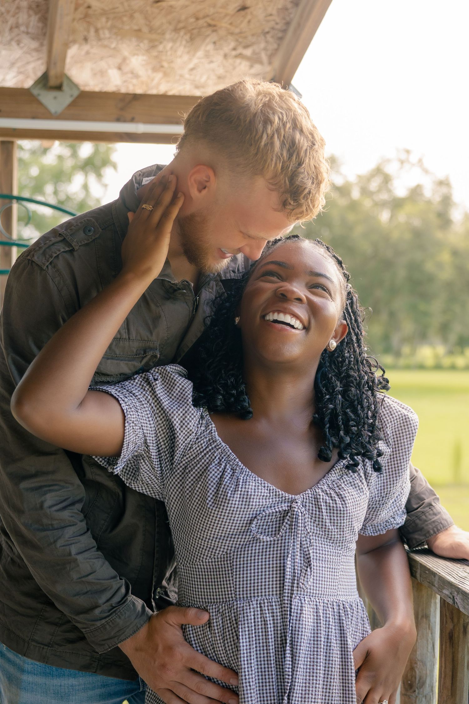 Happy interracial couple sharing a tender moment outdoors, woman laughing joyfully as man whispers in her ear.