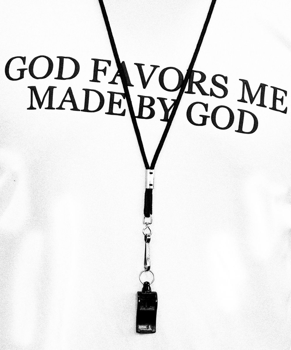 Close-up of a white shirt reading God Favors Me Made By God with a black lanyard and whistle.