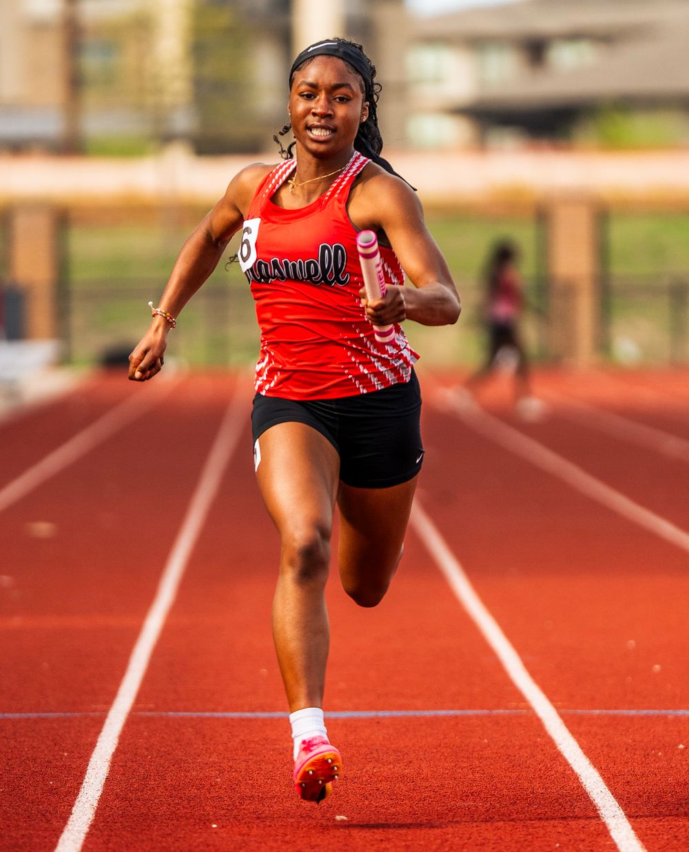 A young female sprinter in a red Roswell uniform races down a track during a competitive track meet.