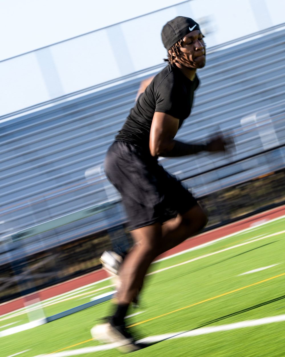 An athlete in all black sprints across a turf field with motion blur emphasizing speed and athleticism.