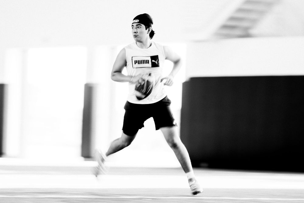 Athlete in Puma gear running with football in black and white action shot indoors.