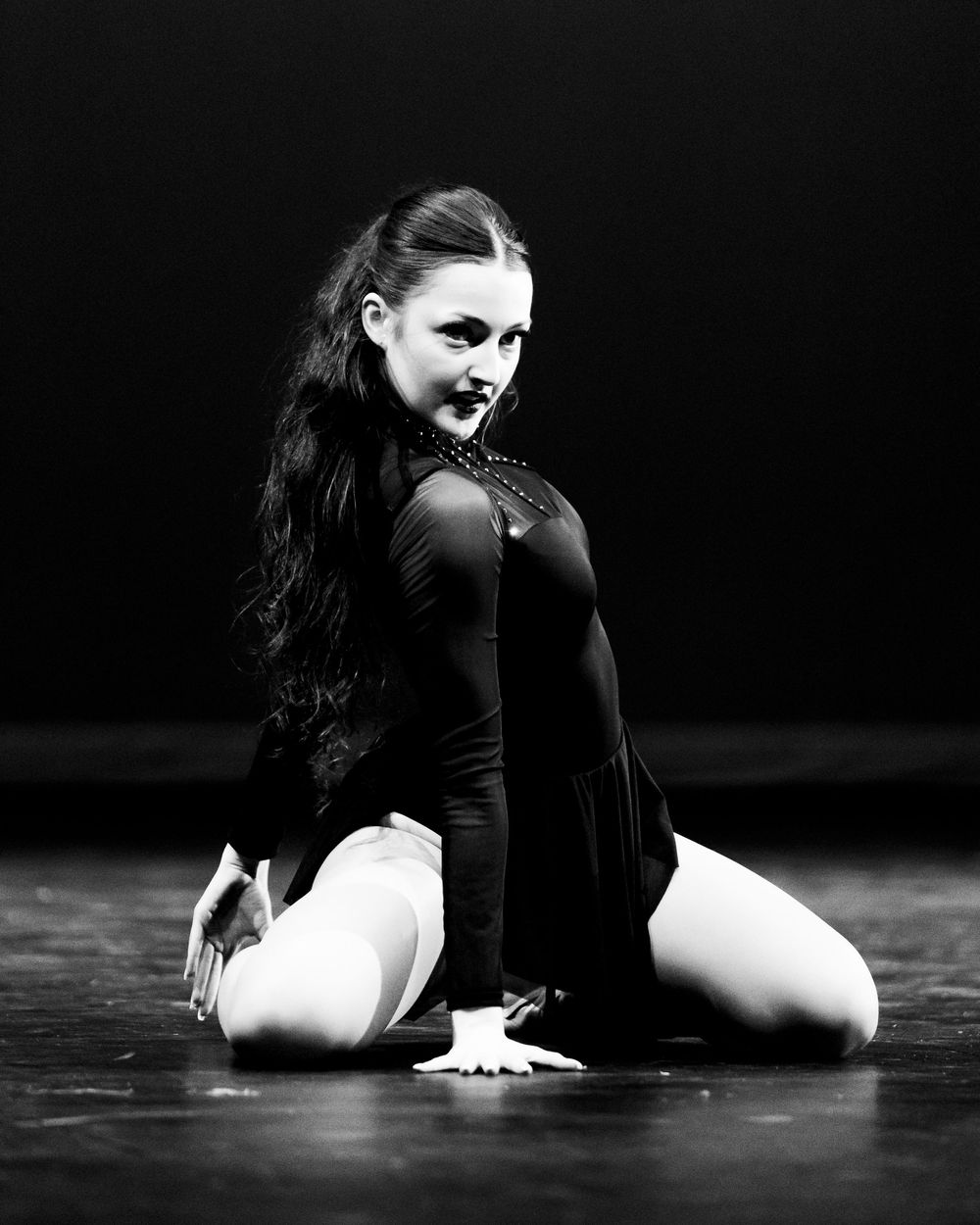 Female dancer in black leotard posing gracefully on stage in dramatic black and white portrait.