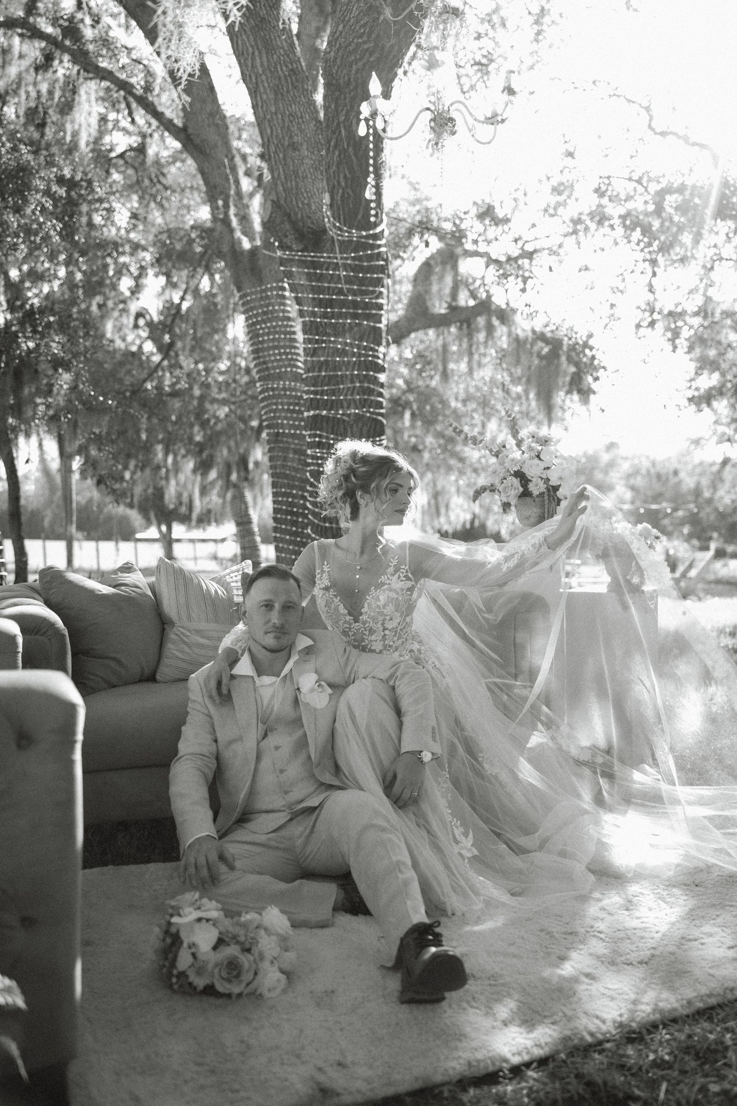 Black and white photo of a bride and groom holding hands walking across a grassy field at dusk.