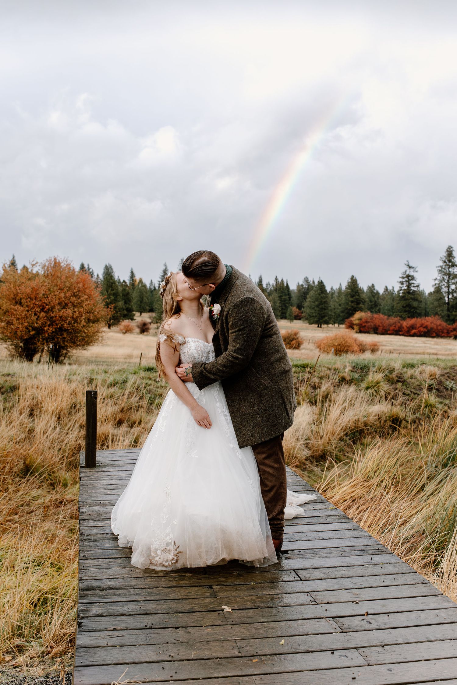 Rainbow behind bride and groom near the pond for some rainy portraits in Oregon