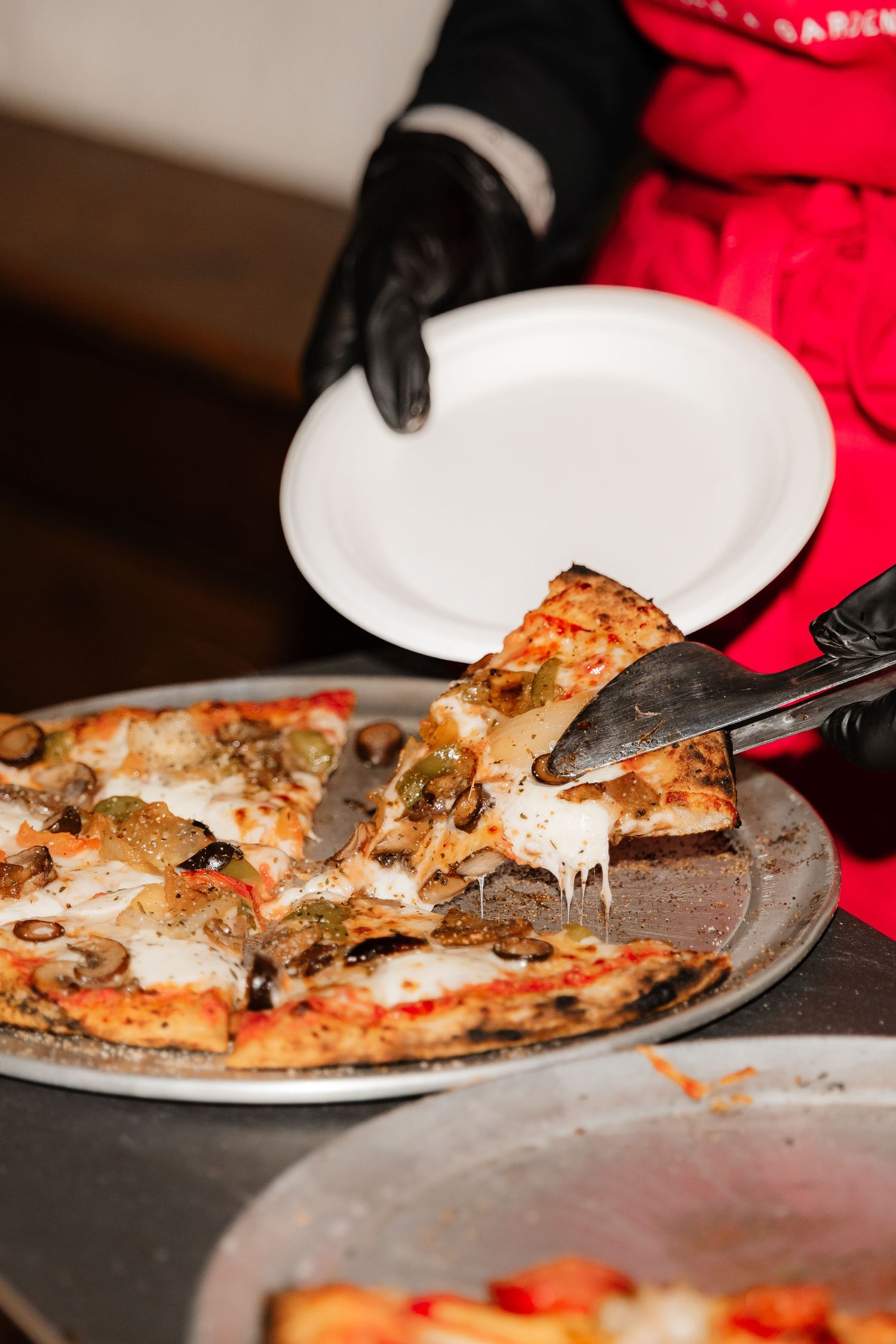 Catering staff serving fresh wood-fired pizza slices with toppings at a wedding reception buffet.