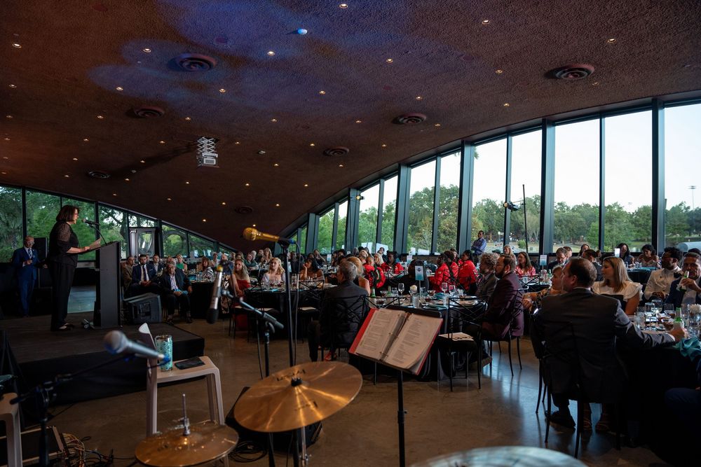 Elegant gala dinner event in a modern venue with panoramic windows, round tables, and live orchestra.