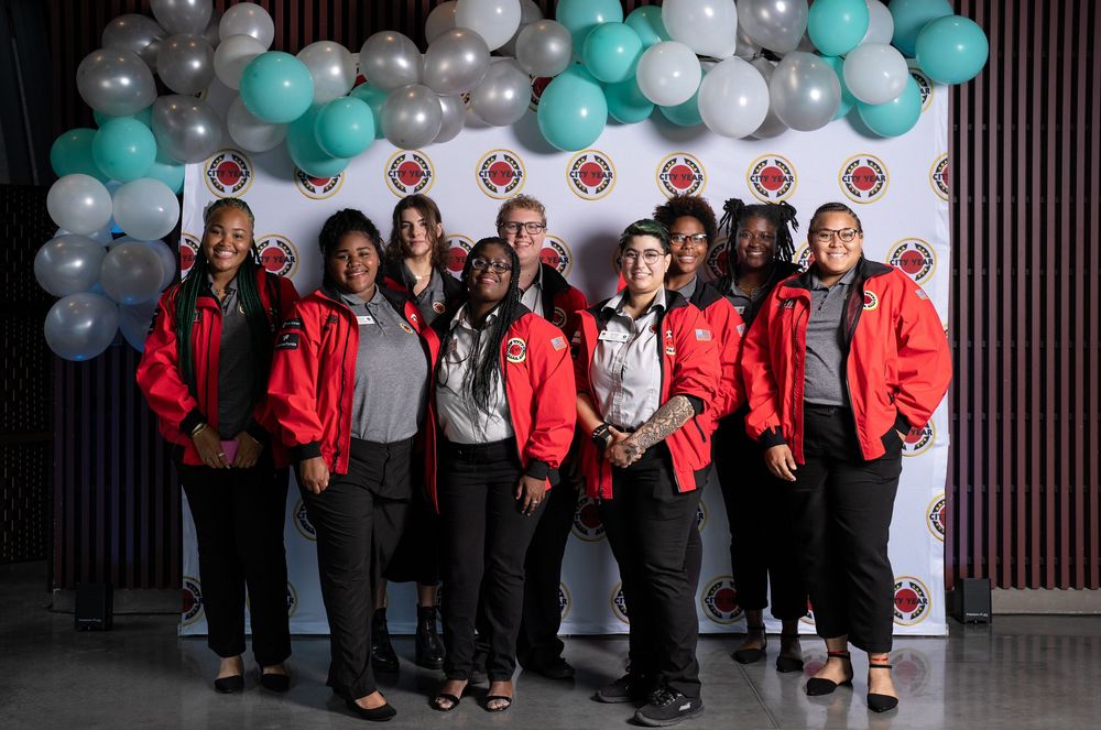 Group of professionals in red jackets posing together in front of a balloon backdrop at a corporate event.