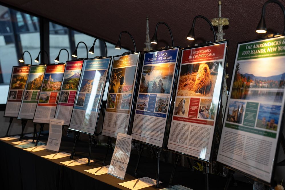 A row of illuminated display boards with colorful travel posters and informational panels at an exhibition event.