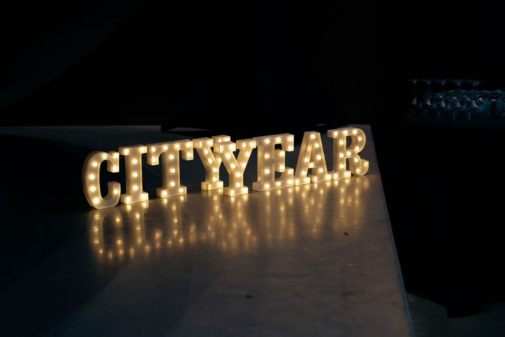 Illuminated marquee letter lights spelling CITYYEAR glowing in the dark on a reflective surface.