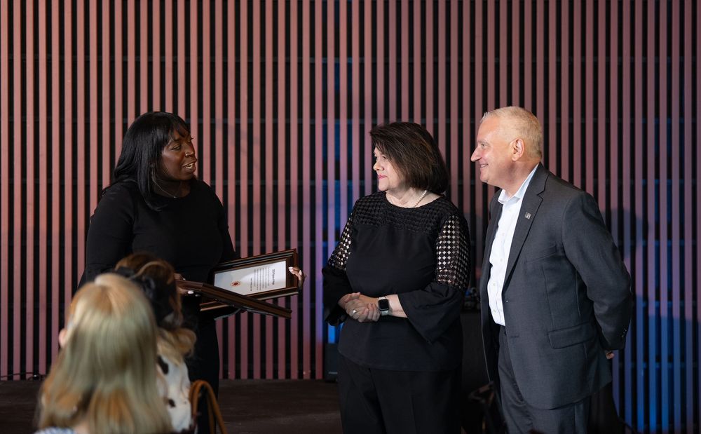 Three professionals engaged in conversation in a modern venue with a wooden slat wall backdrop.