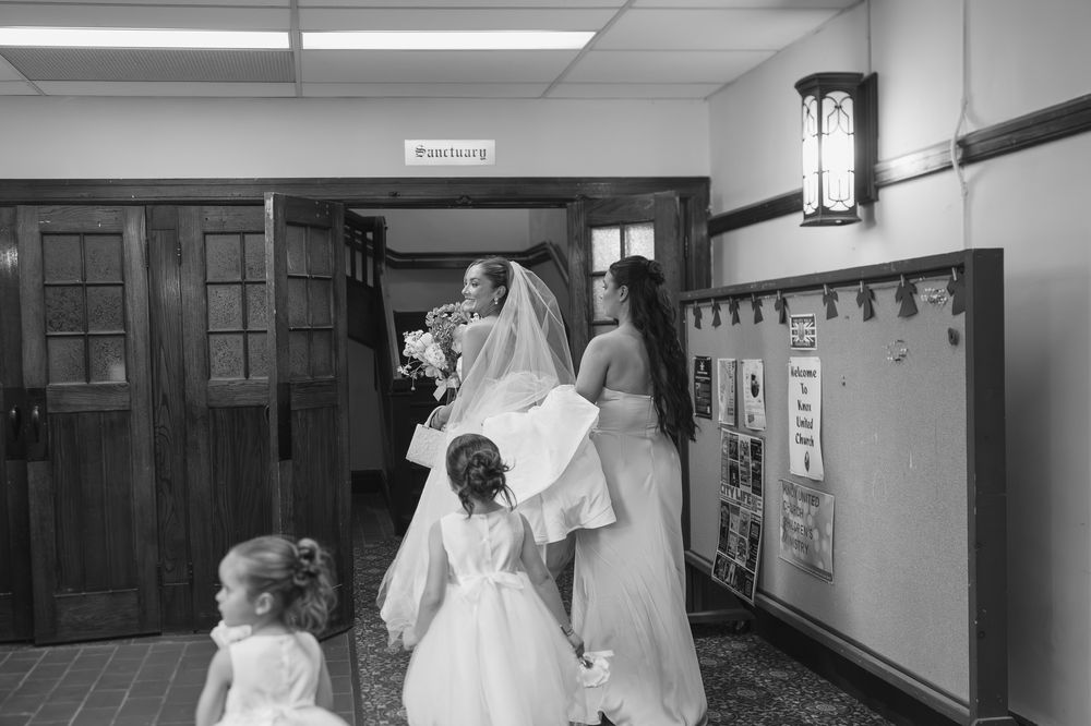 Black and white photo of a bride with flower girls and bridesmaids in a hallway before the wedding ceremony at the Knox Church, Saskatoon