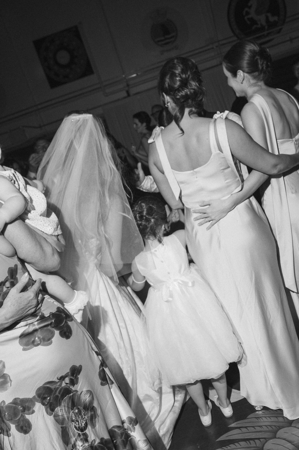 Black and white wedding photo showing bride with veil, bridesmaids, and flower girl in white dresses at reception.