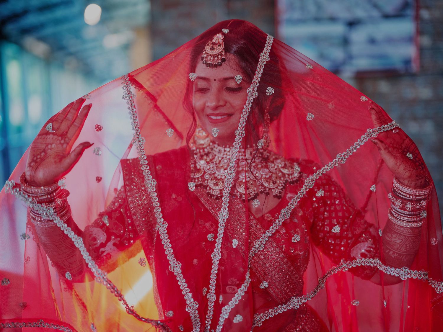 A radiant Indian bride in a red lehenga and dupatta adorned with silver embroidery poses gracefully on her wedding day.