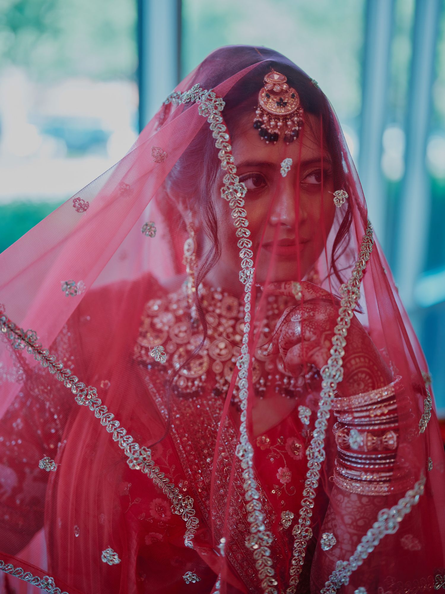 Indian bride in red embroidered lehenga and dupatta veil with ornate bridal jewelry closeup portrait.