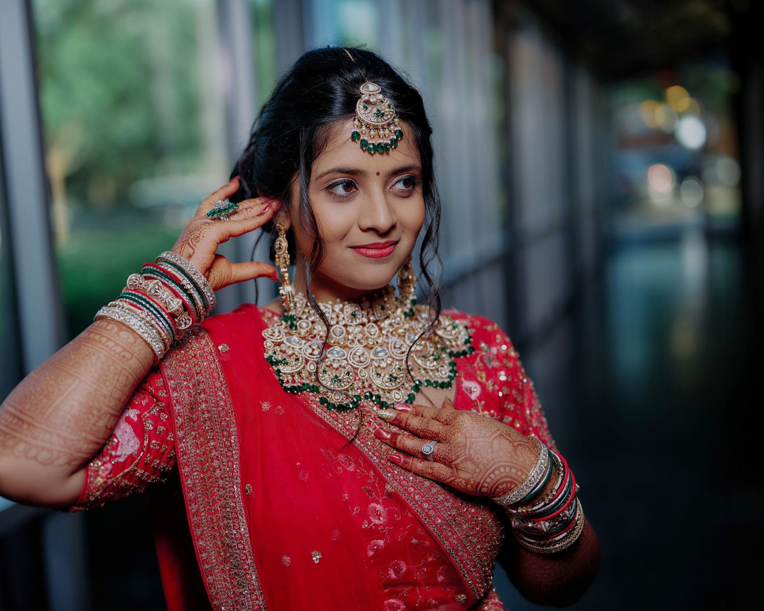 Indian bride in red lehenga with gold jewelry and maang tikka posing elegantly for wedding photography.
