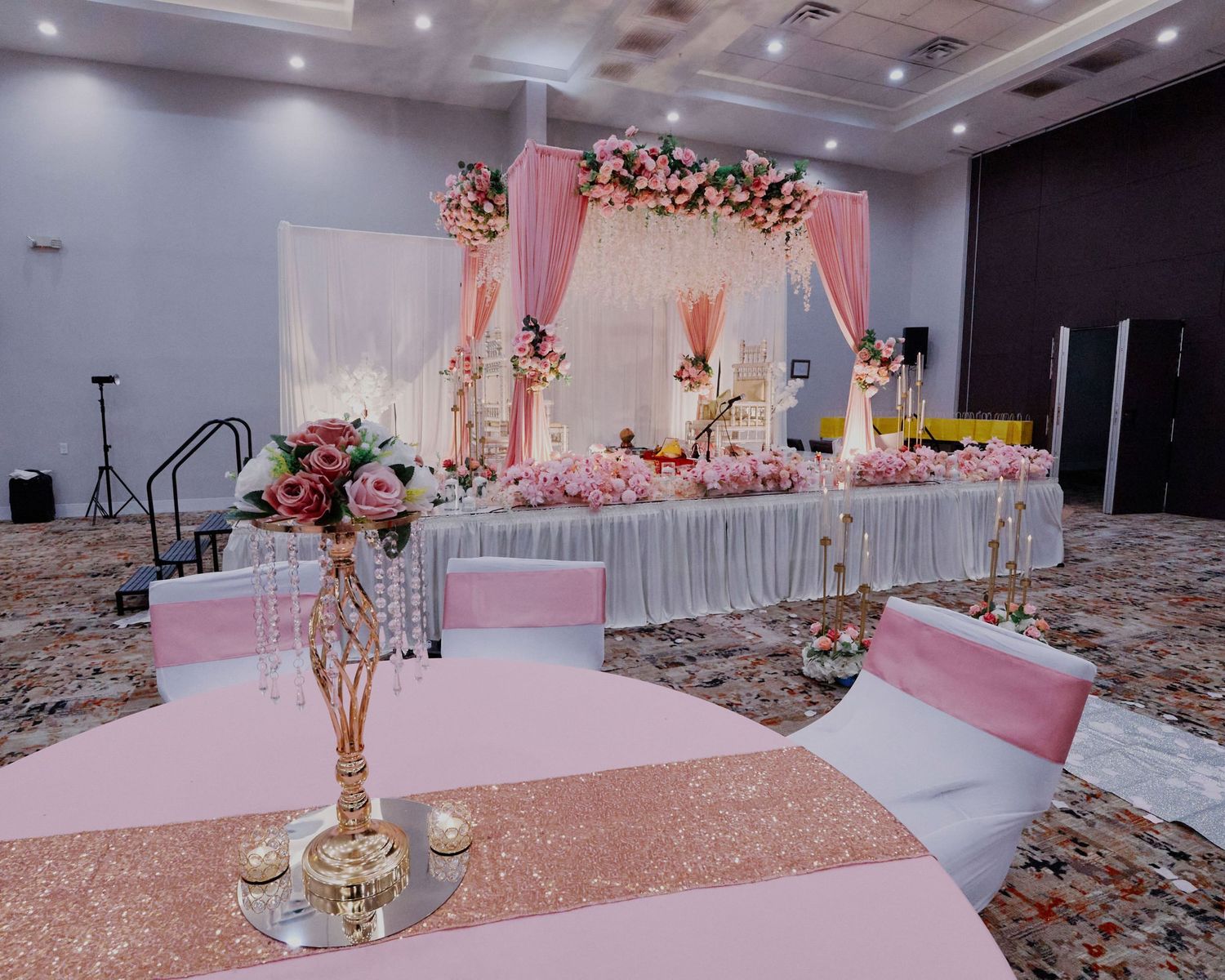 Elegant Indian wedding reception hall decorated in pink and white with floral centerpieces and mandap backdrop.