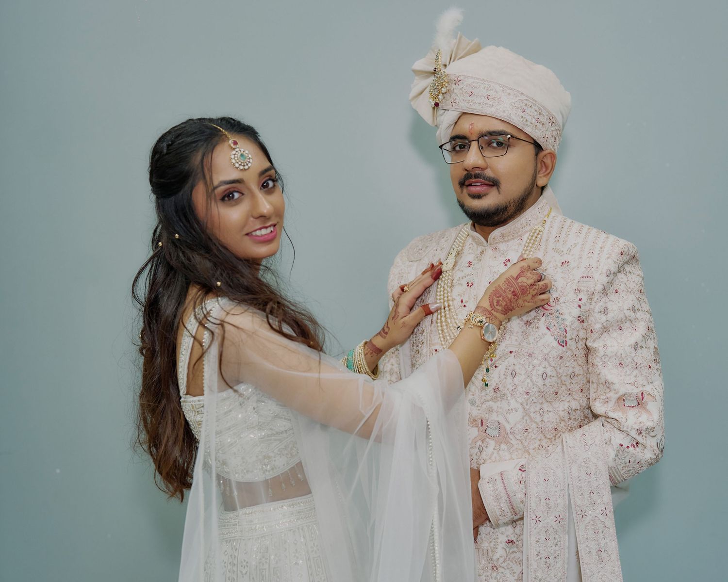 Indian bride and groom in white wedding attire posing together during traditional Hindu wedding ceremony.