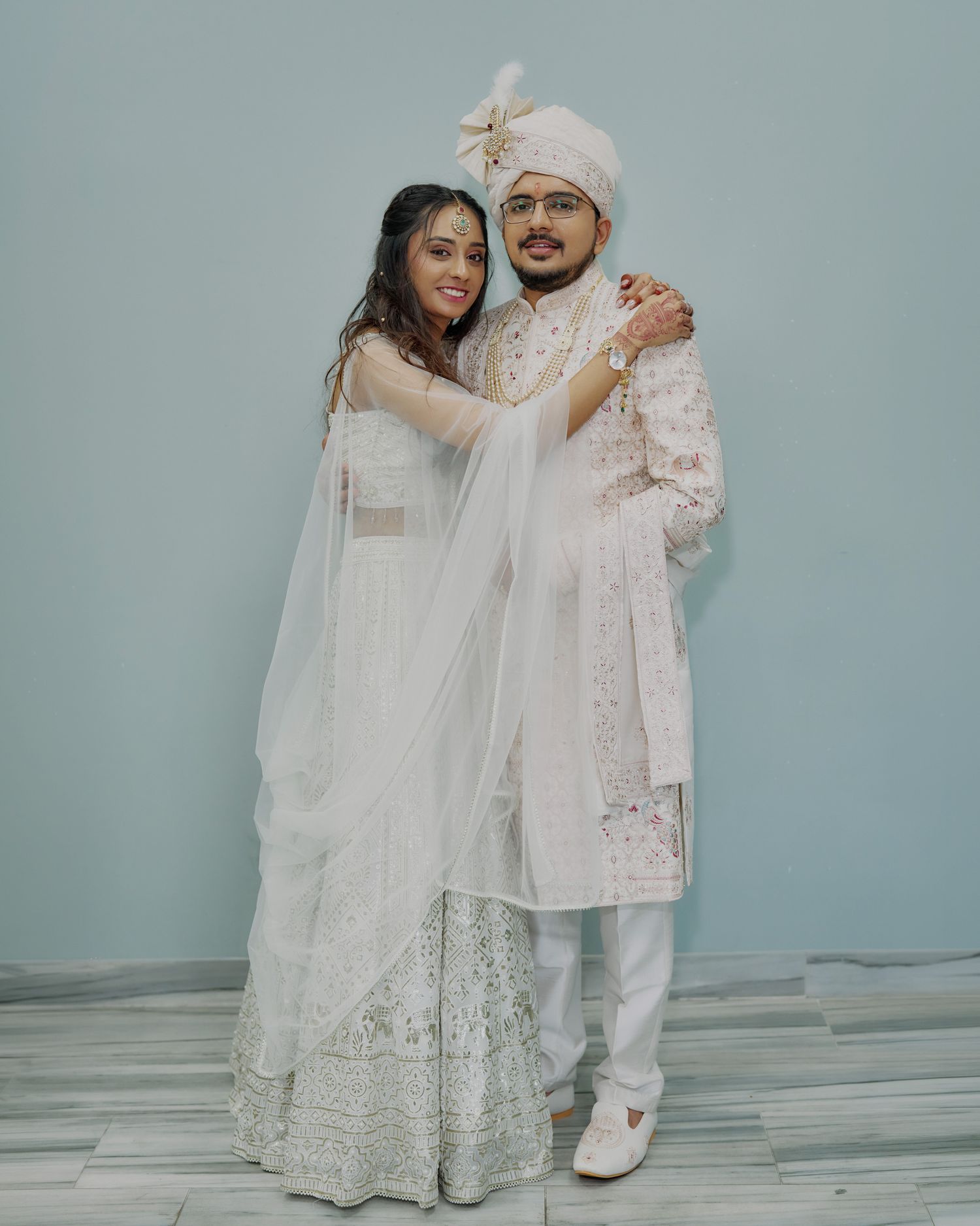 Couple in matching white Indian wedding attire embrace for elegant nikah or engagement ceremony portrait.