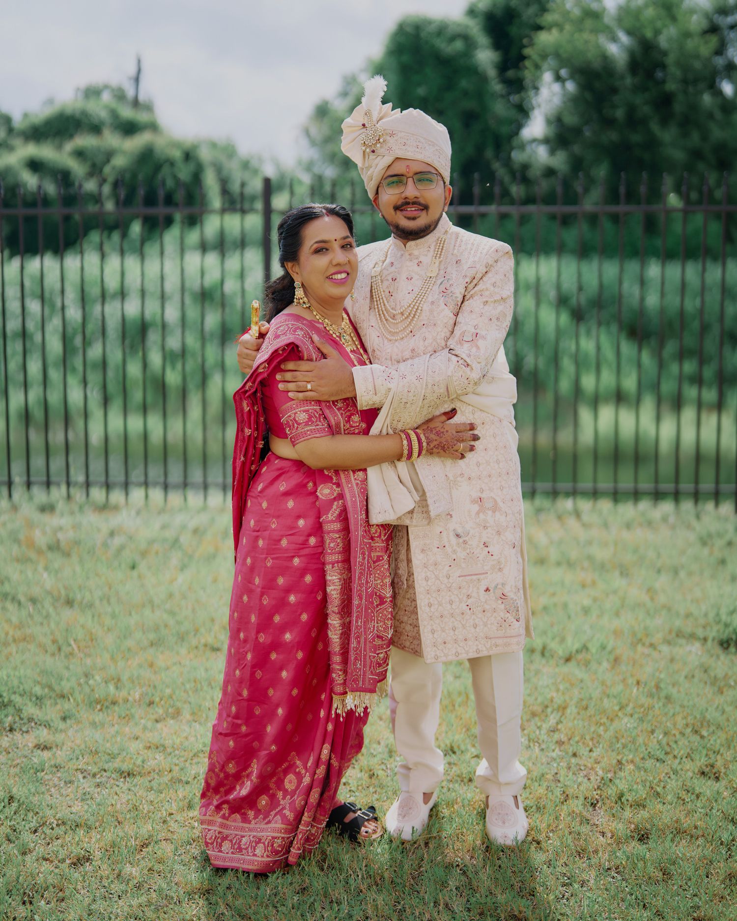 Indian bride and groom in pink saree and ivory sherwani embracing outdoors at wedding celebration.