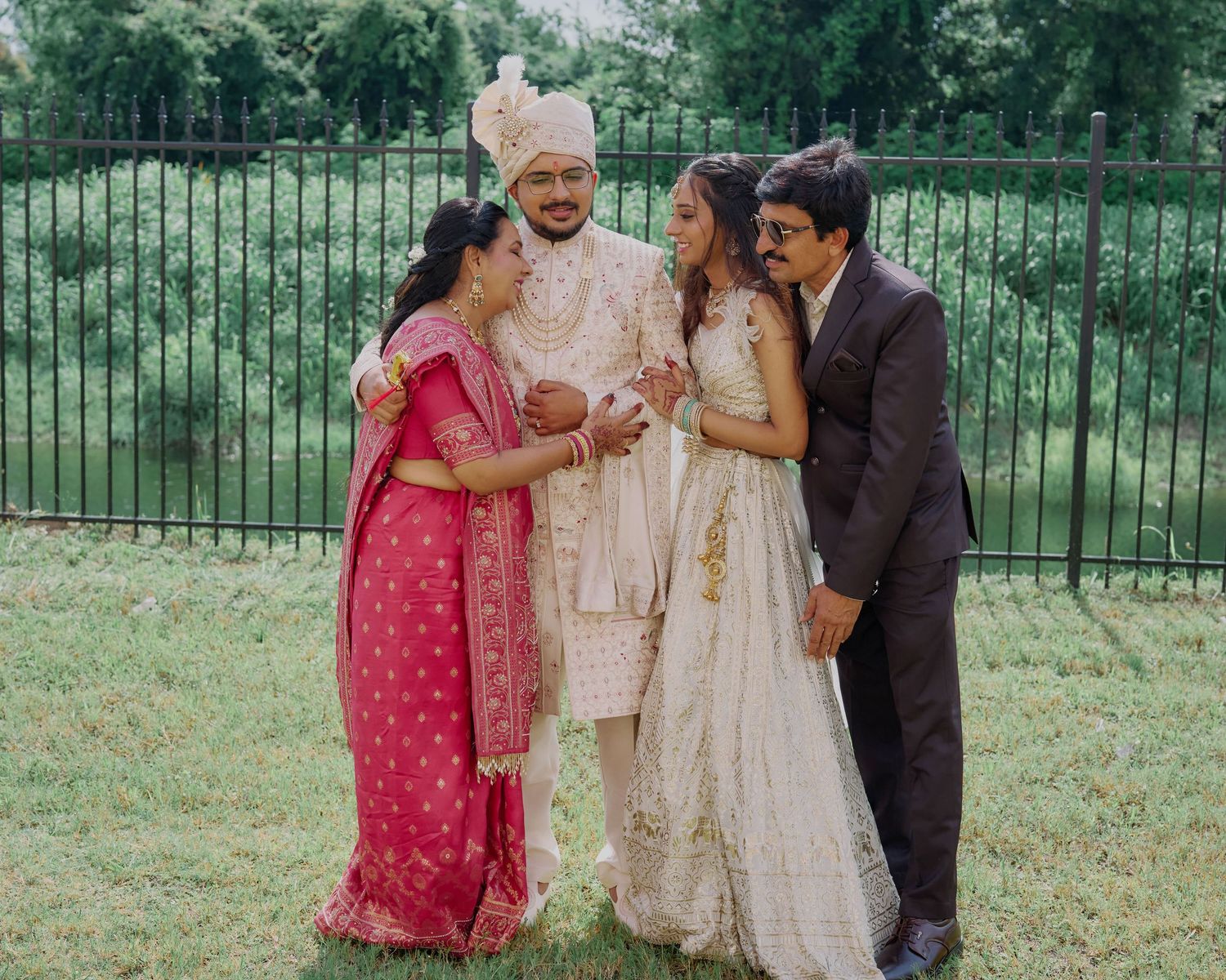 Indian wedding family portrait with bride groom and parents in traditional attire outdoors.