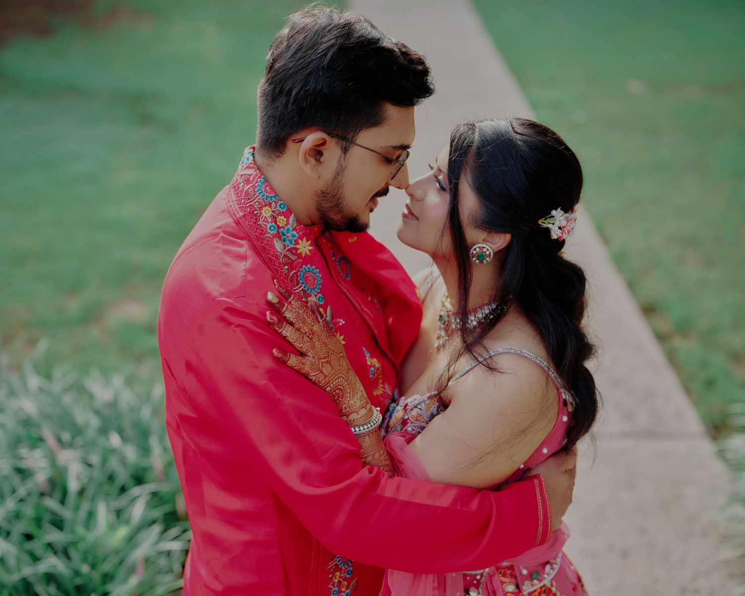 Couple in matching red traditional Indian outfits sharing a romantic moment outdoors.