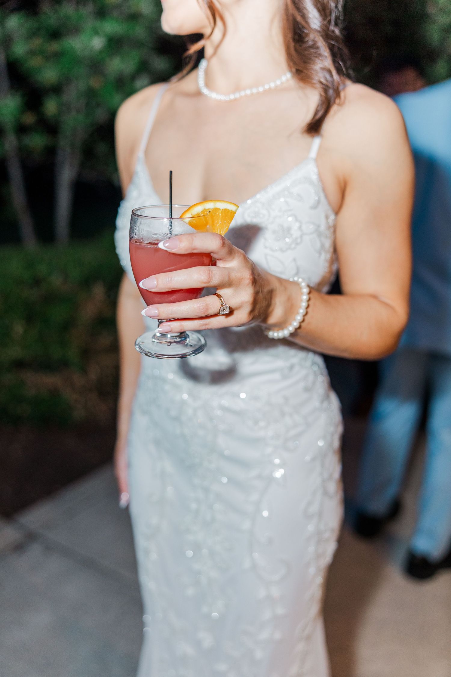 Bride in sequin gown holding a pink cocktail garnished with orange slice at wedding reception.