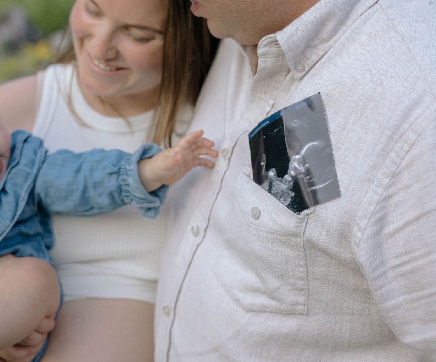Couple sharing tender moment with toddler as father displays ultrasound photo in shirt pocket.