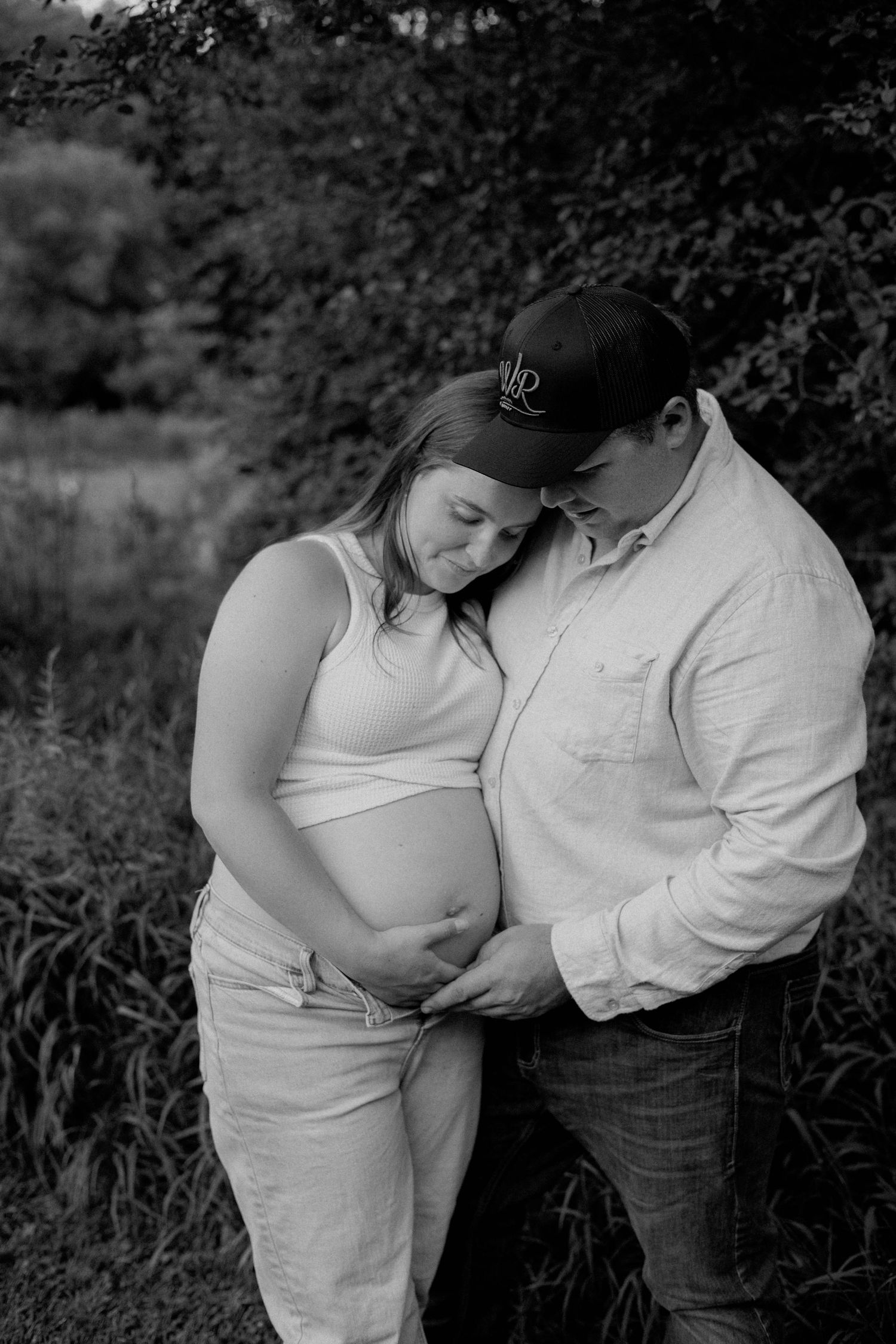 Black and white photo of expecting couple tenderly holding pregnant belly in nature.