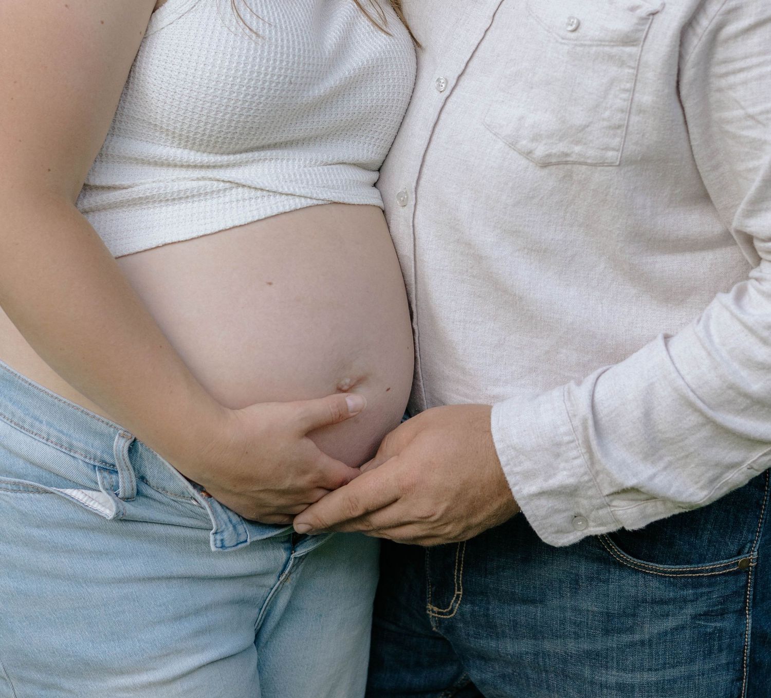 Close-up of pregnant woman's bare belly with partner's hand gently resting beside it.