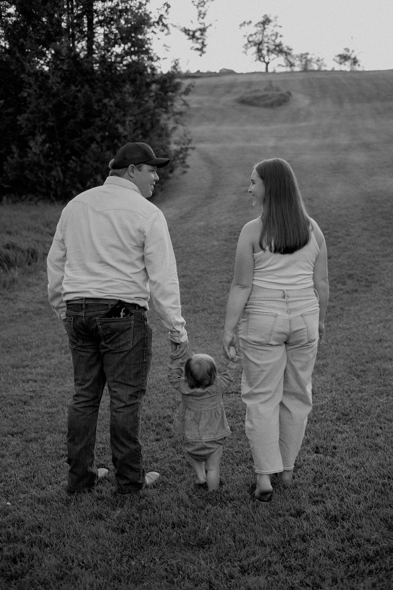 Black and white photo of couple walking with toddler on grassy hillside path.