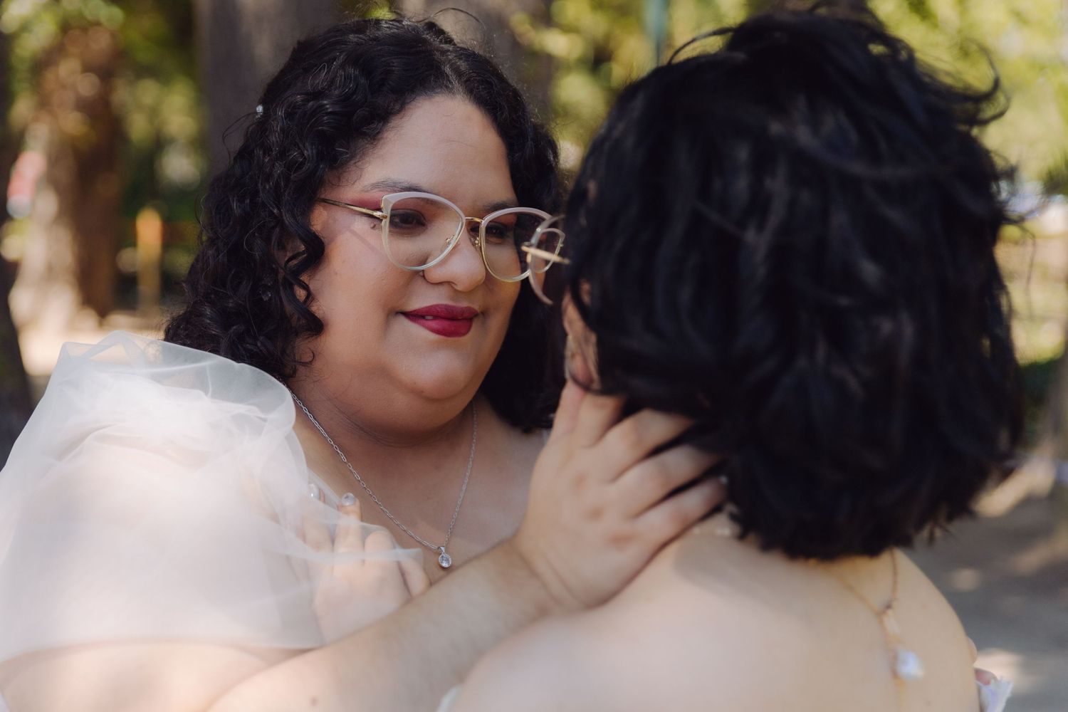 Close-up portrait of two brides in an affectionate embrace, one wearing cat-eye glasses and red lipstick.